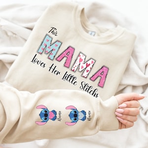 May include: A beige sweatshirt with the text "This Mama Loves Her Little Stitchs" in pink and blue letters with hearts. The sleeves have a blue Stitch character with pink hearts.