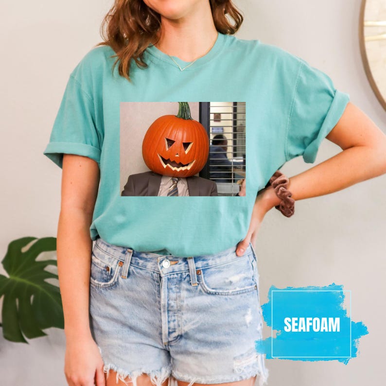 May include: A teal blue t-shirt with a graphic of a person wearing a jack-o-lantern on their head. The graphic is from the TV show "The Office".