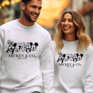 May include: White crewneck sweatshirts with a black and white graphic print of Mickey Mouse and friends. The text "MICKEY & CO. EST. 1928" is printed below the graphic.
