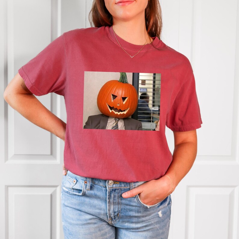 May include: A maroon t-shirt with a graphic of a person wearing a carved pumpkin as a head. The pumpkin has a scary face and the person is wearing a suit and tie. The graphic is set against a white background.