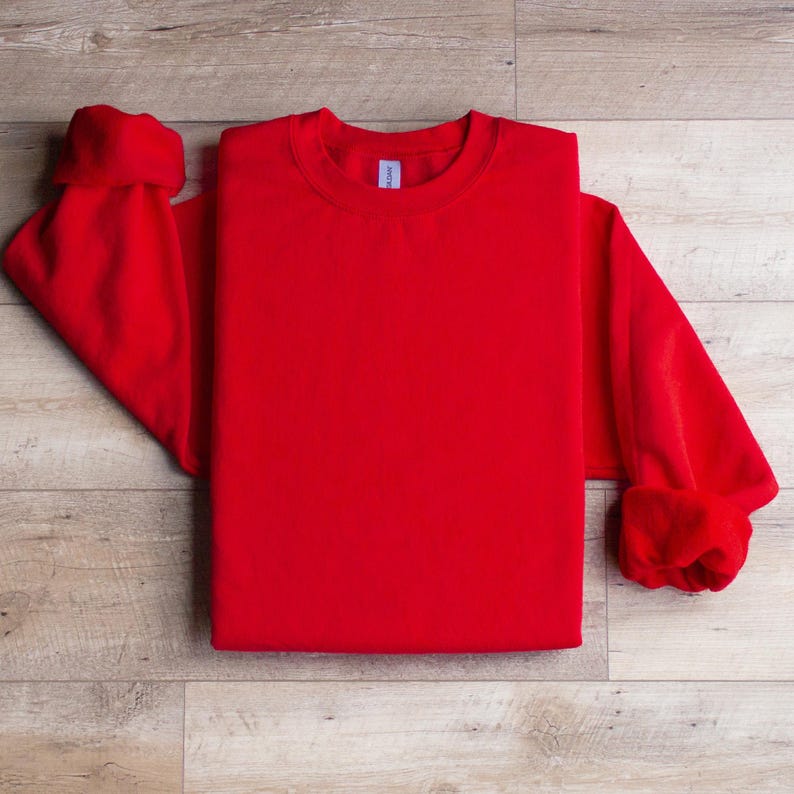 Puede incluir: Una sudadera roja de cuello redondo doblada sobre una superficie de madera. La sudadera es lisa y no tiene ning&uacute;n dise&ntilde;o.