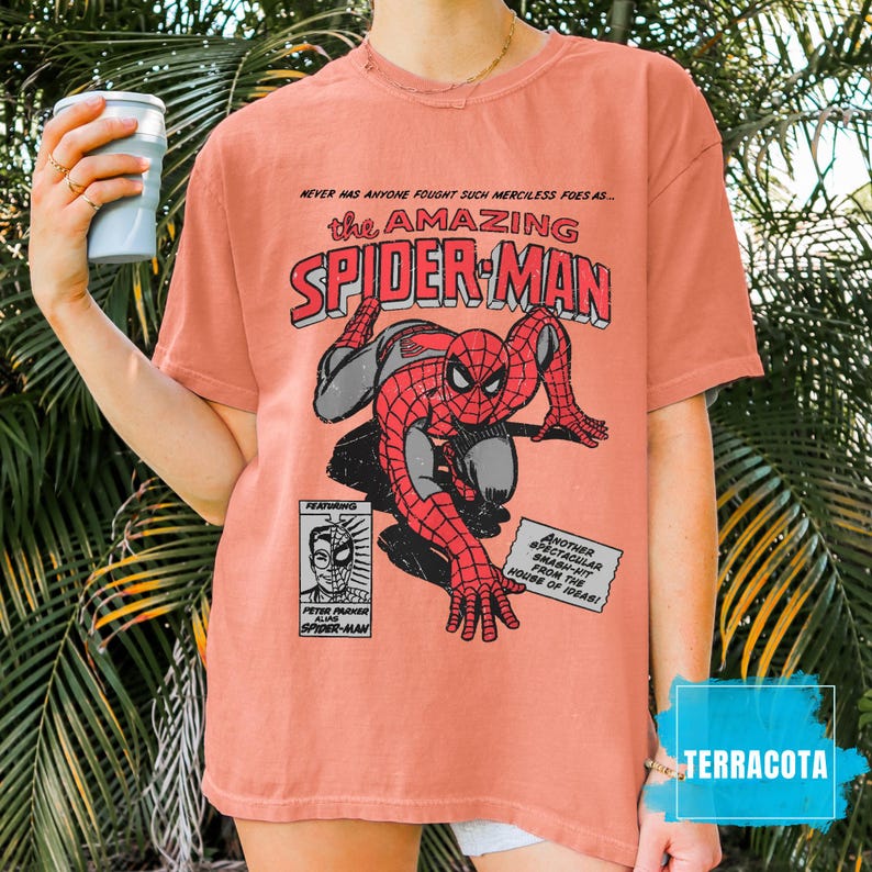 May include: Terracotta-colored t-shirt featuring a comic book graphic of Spider-Man. The design includes the text "the AMAZING SPIDER-MAN" and other comic book elements. The shirt has short sleeves and a relaxed fit.