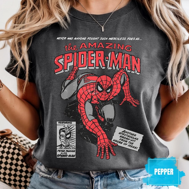 May include: Dark gray t-shirt featuring a vintage comic book cover design of Spider-Man. The graphic includes the text "the AMAZING SPIDER-MAN" in red and white, with additional text and a small image of Peter Parker.