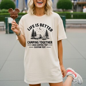 Puede incluir: Camiseta color crema con el texto negro "LIFE IS BETTER CAMPING TOGETHER". El dise&ntilde;o incluye una tienda de campa&ntilde;a, &aacute;rboles y una luna. Debajo, se lee "2026 CAMPING TRIP - CUSTOM TEXT".