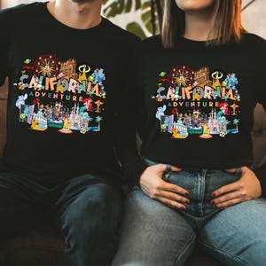 May include: Black long-sleeve shirts with a colorful graphic that reads "California Adventure." The graphic includes a Ferris wheel, castle, and various cartoon characters. The shirts are a comfortable, casual style.