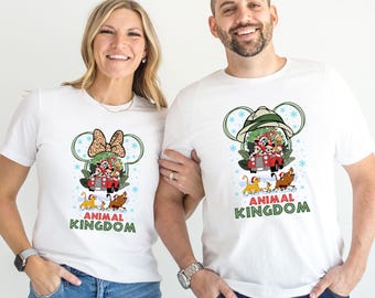 May include: White t-shirts with a graphic featuring a red car carrying Disney characters inside a snow globe. The design includes the text "ANIMAL KINGDOM" in green. One shirt has a Minnie Mouse bow, the other a safari hat.