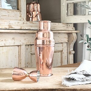 May include: A set of copper cocktail shakers and jiggers. The shaker has a hammered finish and a classic design. The jigger is a double-ended measuring cup.