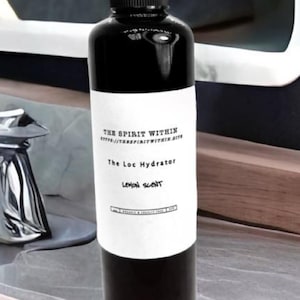 May include: Black bottle of The Loc Hydrator with a white label. The label includes the text "THE SPIRIT WITHIN", "The Loc Hydrator", and "Lemon Scent". The bottle has a black spray nozzle and is on a light-coloured surface.
