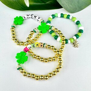 May include: Three gold bead bracelets with green shamrock charms and letter beads spelling "LUCKY".