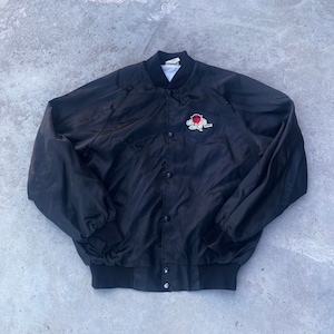 Puede incluir: Una chaqueta bomber de satén negro con cierre de presión y un logotipo bordado en rojo y blanco en el pecho izquierdo. El logotipo presenta un personaje de dibujos animados sosteniendo una pelota de baloncesto.