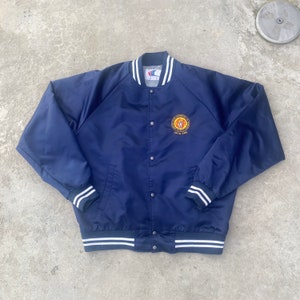 May include: A navy blue satin bomber jacket with white ribbed trim. The jacket has a button closure and features an embroidered patch on the left chest with the text "International Brotherhood of Electrical Workers Local 581".