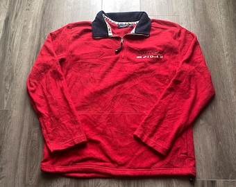 May include: Red fleece pullover with a quarter zip closure and a Nautica logo with small flags. The collar is black with a white and blue trim.