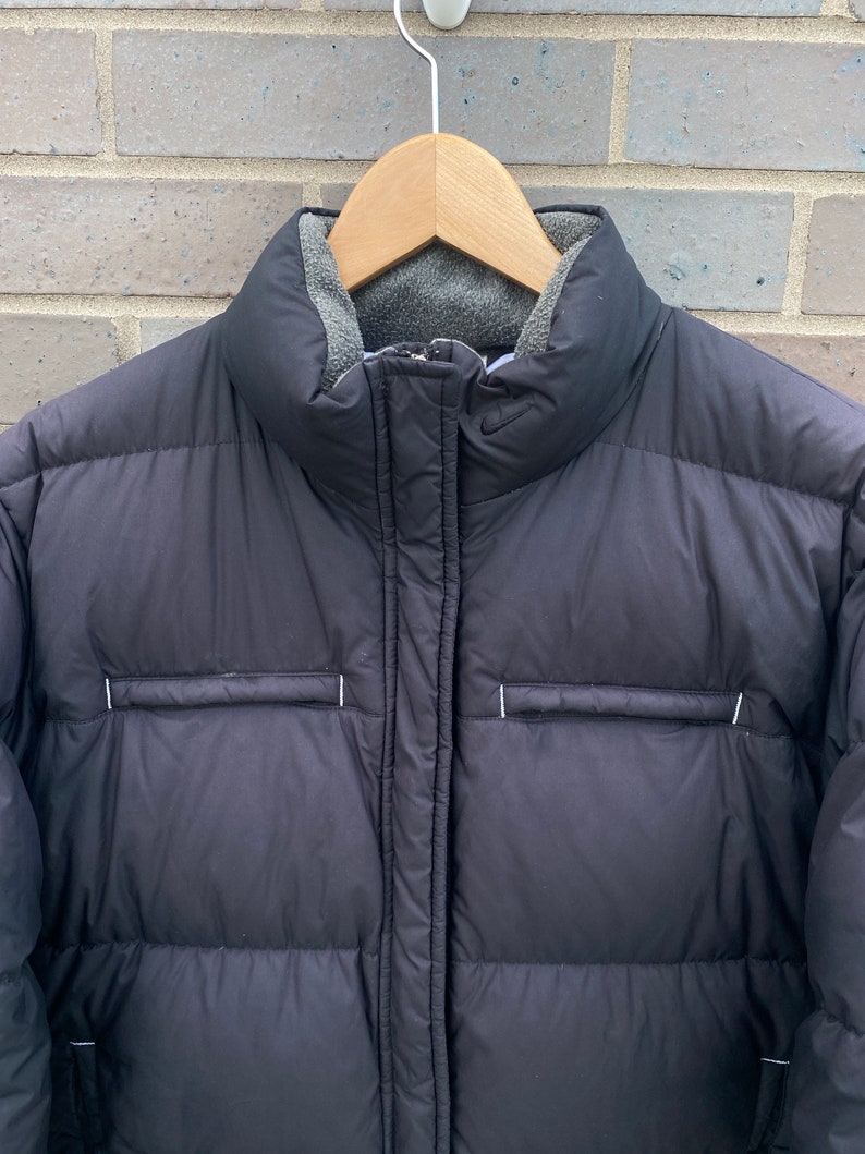 May include: Black puffer jacket with a zipper closure and a fleece lining. The jacket has a quilted design and a small logo on the chest.
