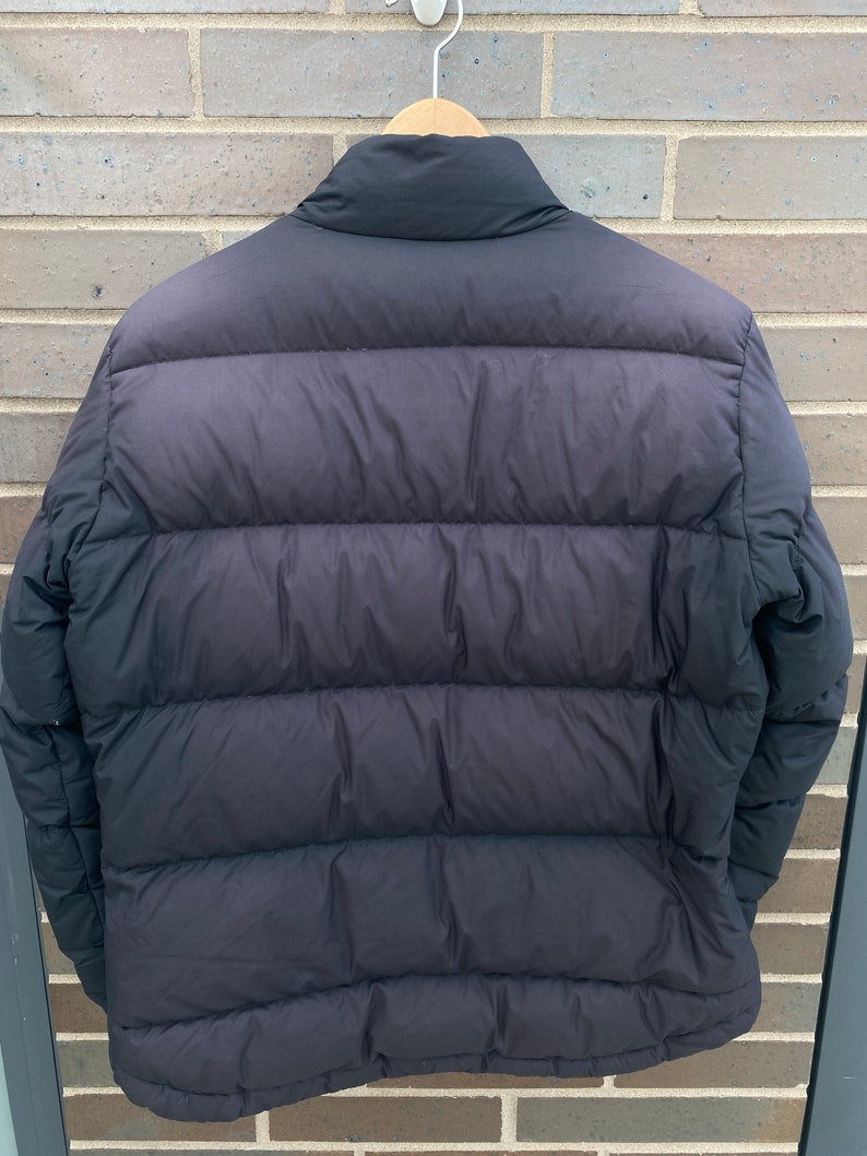 May include: A black puffer jacket with a high collar and a zipper closure. The jacket has a quilted design and is made of a lightweight material.