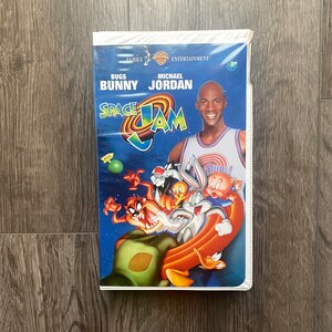 May include: A VHS tape featuring the movie Space Jam with Bugs Bunny and Michael Jordan on the cover. The cover is white with blue and red accents. The title "Space Jam" is in large, bold letters. The characters Bugs Bunny, Tweety Bird, Taz, and Porky Pig are featured on the cover.