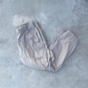 May include: A pair of light grey cargo trousers folded on a grey concrete surface.