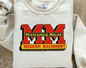 May include: Beige sweatshirt featuring a red and yellow logo that reads "Minneapolis-Moline" and "Modern Machinery" with the text "Tractors-Power Units-Farm Machinery-Implements" below.