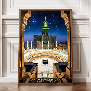 May include: A framed print depicting the Great Mosque of Mecca at night. The image showcases the Kaaba, surrounded by worshippers, with a towering clock tower and a crescent moon in the night sky. The artwork is framed in a wooden border.