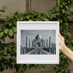 May include: A framed black and white drawing of the Taj Mahal, a famous mausoleum in India. The drawing depicts the building with its intricate details and the surrounding gardens.