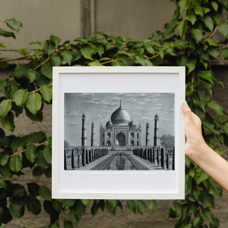 May include: A framed black and white drawing of the Taj Mahal, a famous mausoleum in India. The drawing depicts the building with its intricate details and the surrounding gardens.