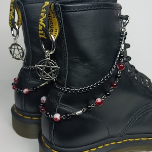 May include: Black leather boots with yellow and black straps, adorned with silver chains, pentagram charms, and red and white beads.