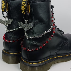May include: Black leather boots with silver chain and red bead accents. The boots have a butterfly charm on each side.
