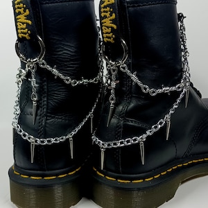 May include: Black leather boots with silver chains and spikes attached to the back. The chains are made of barbed wire and have a cross charm.