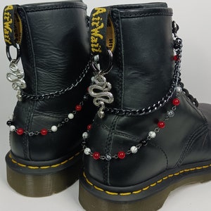 May include: Black leather boots with silver snake charms and red, white, and black beaded chains. The boots have a yellow tag with the text "AirWair" on them.