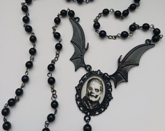 May include: Black beaded necklace with a cameo pendant featuring a man's face and two bat wings. The pendant is framed in a black metal filigree.