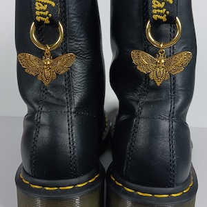 May include: Black leather boots with gold butterfly charms attached to the laces. The boots have yellow stitching and a black rubber sole.