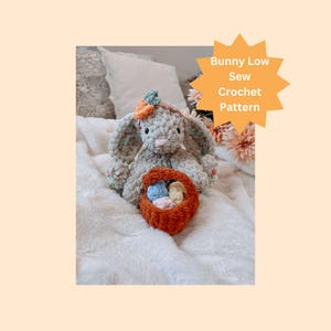 May include: A crocheted bunny holding a basket of colorful eggs. The bunny is gray with a floral pattern and has a small orange flower on its head. The basket is orange and the eggs are blue, pink, and yellow. The bunny is sitting on a white blanket. Bunny Low Sew Crochet Pattern.