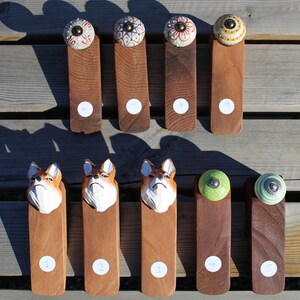 May include: Nine wooden doorstops with different decorative tops. The tops include ceramic knobs with floral patterns, green ceramic knobs, and wooden carvings of a dog's head. The doorstops are numbered 1 through 9.