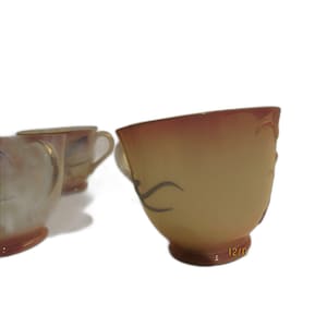 Op de afbeelding: Een set vintage theekopjes met een crème- en perzikkleurverloop. De kopjes hebben een decoratief ontwerp en kleine handvatten. De kopjes zijn in een groep gerangschikt, met één kopje op de voorgrond en andere erachter.