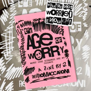 Könnte beinhalten: Ein rosafarbenes Zine mit dem Titel The Age of Worry mit schwarzem, handgezeichnetem Text und Gribbeln. Das Cover enthält den Text Worst Case Scenarios Are My Favorite, A Zine By Z und Retromaccaroni. Ein Aufkleber zeigt You're Not Worried Enough.