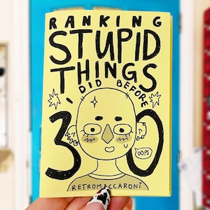 Könnte beinhalten: Ein gelbes Zine mit handgezeichneten schwarzen Illustrationen und dem Text RANKING STUPID THINGS I DID BEFORE 30. Das Cover zeigt eine stilisierte Figur mit Piercings, eine große Zahl 30 und eine kleine Sprechblase mit dem Wort OOPS.