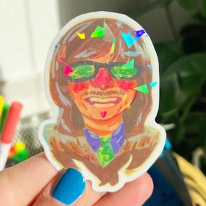 May include: A holographic sticker depicting a colourful illustration of a person wearing sunglasses, a moustache, and a patterned tie. The sticker has a white border and is likely for decorative use.