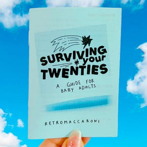 May include: A light blue booklet titled Surviving Your Twenties: A Guide for Baby Adults by Retromaccaroni. The cover features a black hand-drawn shooting star graphic and bold black text centered on the front, with a soft blue horizontal line.