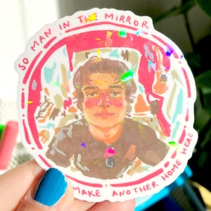 以下が含まれることがあります： 茶色の髪と黒いシャツを着た人のイラストが描かれたステッカー。ステッカーは赤い縁取りで、「SO MAN IN THE MIRROR」と「MAKE ANOTHER HOME HERE」の文字が入っています。ステッカーはホログラフィック効果があります。