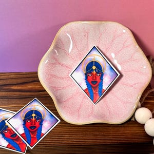 Puede incluir: Una pegatina con una ilustración digital de una mujer con cabello azul, que lleva una corona dorada y una diadema azul. El fondo es un patrón de galaxia con estrellas y una luna creciente.