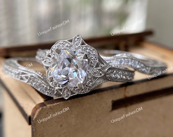 May include: A silver engagement ring set with a large, clear, square-shaped center stone surrounded by smaller stones. The ring is set in a delicate floral design. The band is also adorned with smaller stones.