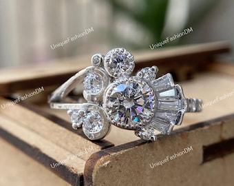 May include: A silver ring with a large round center stone and smaller stones set in a floral design. The ring is set in a wooden box.