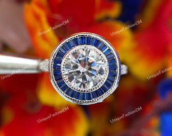 May include: A silver ring with a large round center diamond surrounded by a halo of smaller blue sapphires.