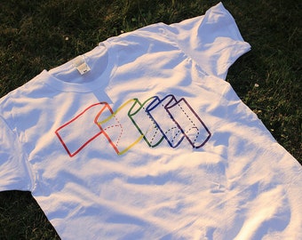 May include: White t-shirt with a rainbow-colored design of a flag made of folded paper.