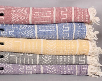 May include: Five patterned towels stacked on top of each other. The towels are red, blue, yellow, gray, and purple. Each towel has a white fringe.