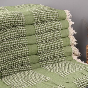 May include: A green waffle weave throw blanket with white fringe. The blanket is folded in a stack and has a textured pattern.