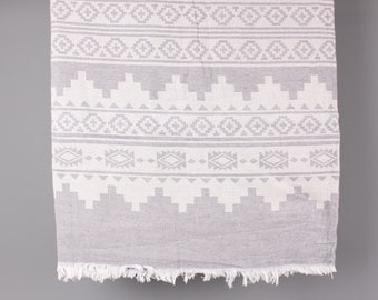 May include: A gray and white patterned textile with a geometric design. The fabric features repeating shapes and patterns, including diamonds, triangles, and squares. The bottom edge has a fringe.