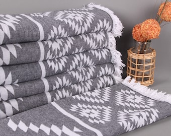 Peut inclure: Une pile de serviettes grises et blanches à motifs avec des bords à franges. Les serviettes présentent un motif géométrique blanc sur fond gris. Des sphères décoratives orange dans un vase en verre sont en arrière-plan.