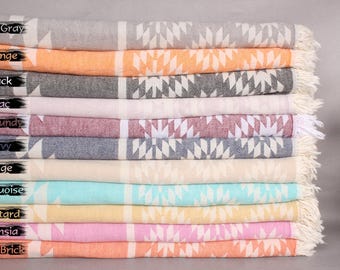May include: A stack of 12 Turkish towels in various colors, including dark gray, orange, black, lilac, burgundy, navy, beige, turquoise, mustard, fuchsia, and dark brick. Each towel features a white geometric pattern.