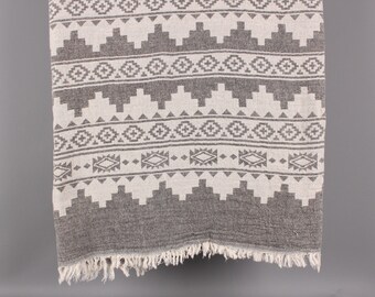 Peut inclure: Textile à motifs gris et blancs avec un motif géométrique. Le tissu a un bord effiloché et un motif de formes répétées. Le textile est probablement une couverture ou un jeté.