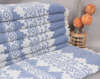 May include: A stack of blue and white patterned Turkish towels with fringed edges. The towels feature a geometric design in light blue against a white background. The towels are folded and stacked, showcasing the pattern.